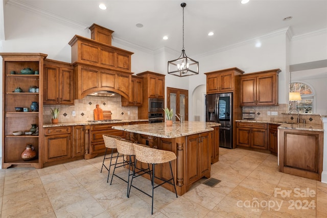 kitchen with light stone countertops, an island with sink, pendant lighting, appliances with stainless steel finishes, and ornamental molding