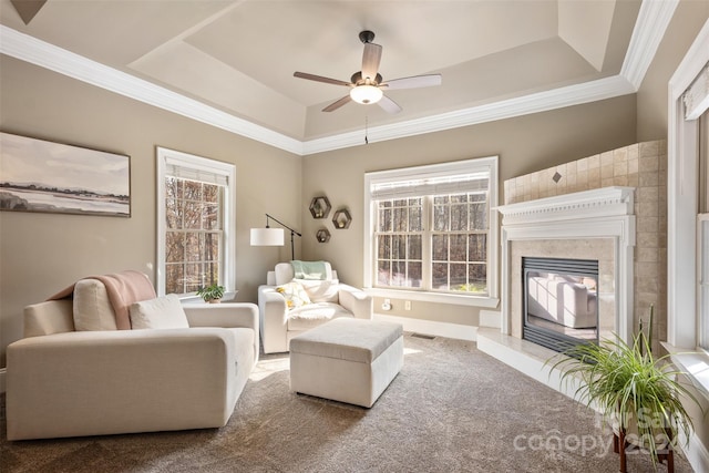 carpeted living room with ceiling fan, ornamental molding, a high end fireplace, and a tray ceiling