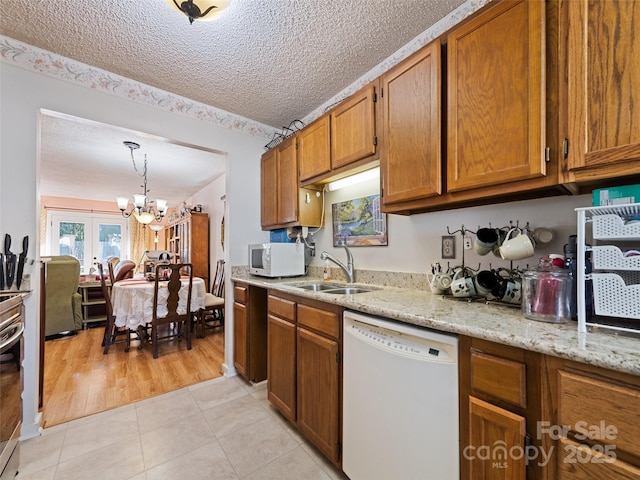 kitchen with light stone counters, a textured ceiling, white appliances, sink, and a notable chandelier