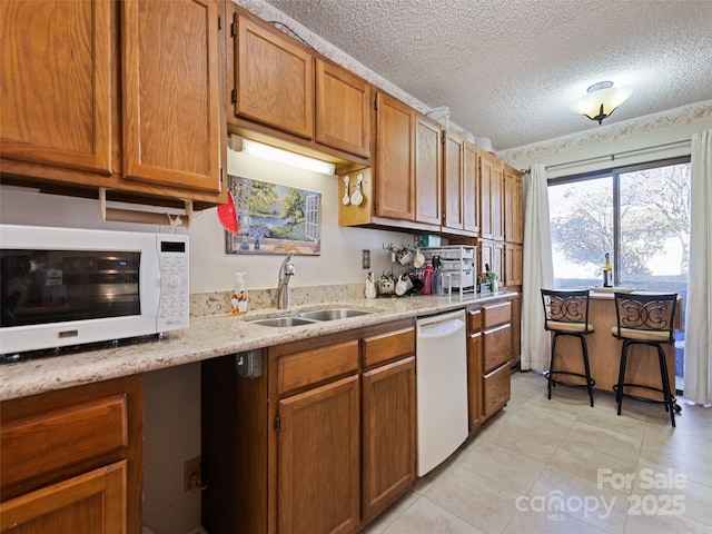 kitchen with light stone countertops, sink, a textured ceiling, white appliances, and light tile patterned floors