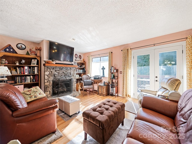 living room featuring a textured ceiling, a fireplace, french doors, and light wood-type flooring