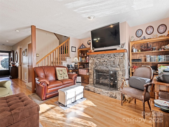 living room featuring hardwood / wood-style flooring, a stone fireplace, and a textured ceiling