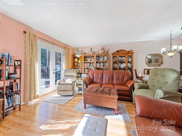 living room featuring a chandelier, french doors, a textured ceiling, and light hardwood / wood-style floors