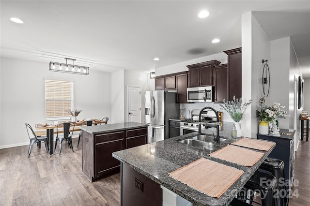 kitchen featuring sink, stainless steel appliances, dark hardwood / wood-style flooring, dark stone countertops, and a kitchen island