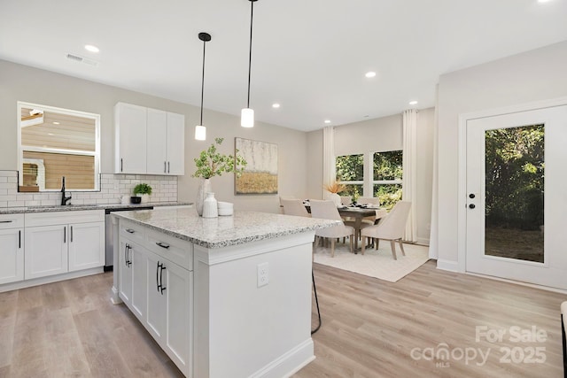 kitchen featuring light stone countertops, sink, white cabinets, and a kitchen island