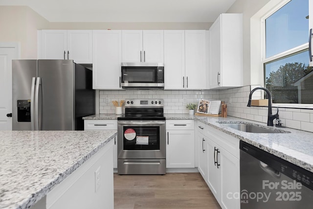 kitchen with sink, decorative backsplash, appliances with stainless steel finishes, light hardwood / wood-style floors, and white cabinetry