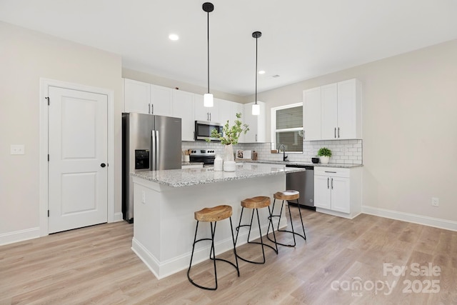 kitchen with light stone countertops, a center island, white cabinets, and appliances with stainless steel finishes