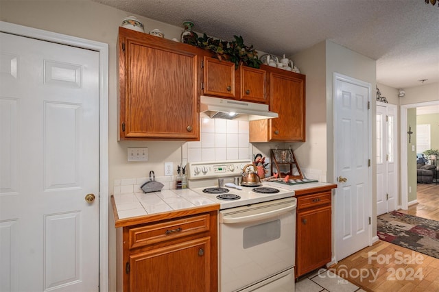 kitchen with a textured ceiling, light wood-type flooring, white range with electric stovetop, and tile counters