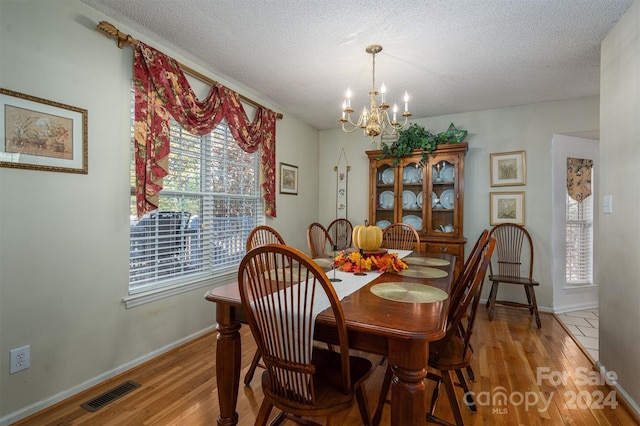 dining area featuring a healthy amount of sunlight, an inviting chandelier, a textured ceiling, and light hardwood / wood-style flooring