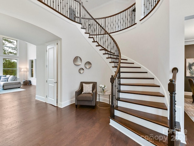 stairway with a high ceiling, crown molding, and wood-type flooring