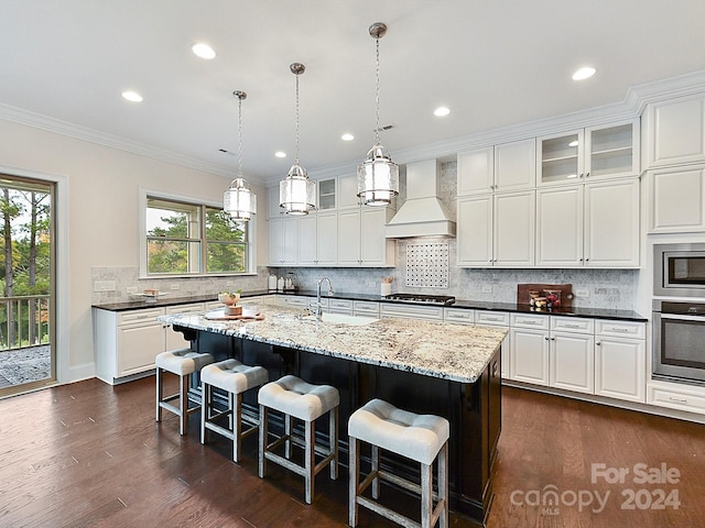 kitchen with premium range hood, a center island with sink, crown molding, dark hardwood / wood-style floors, and stainless steel appliances