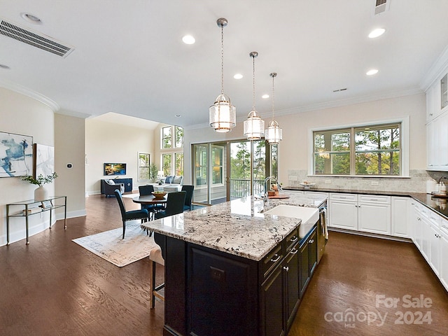 kitchen with decorative backsplash, a kitchen bar, crown molding, dark wood-type flooring, and an island with sink