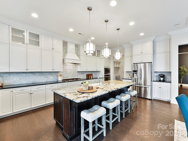 kitchen featuring dark hardwood / wood-style floors, decorative light fixtures, a center island with sink, appliances with stainless steel finishes, and custom exhaust hood