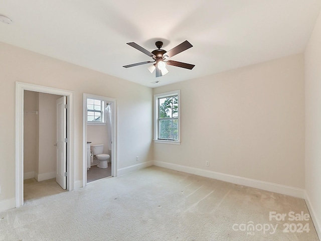 unfurnished bedroom with ceiling fan, light carpet, connected bathroom, and multiple windows