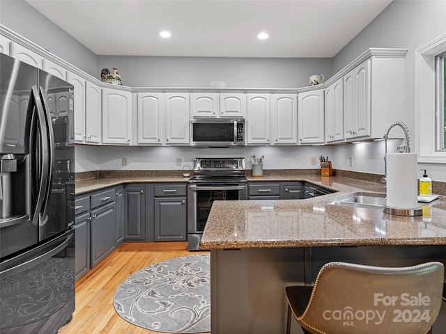 kitchen with sink, stainless steel appliances, light hardwood / wood-style floors, stone countertops, and white cabinets