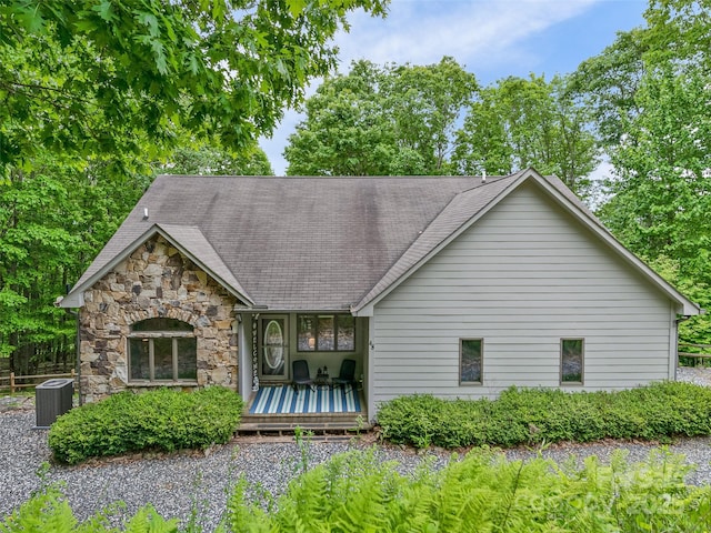 back of house with roof with shingles, central AC, and stone siding