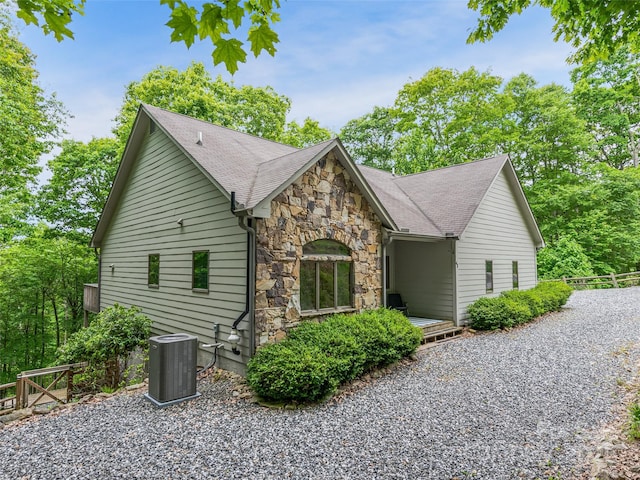 view of home's exterior featuring roof with shingles, fence, stone siding, and cooling unit