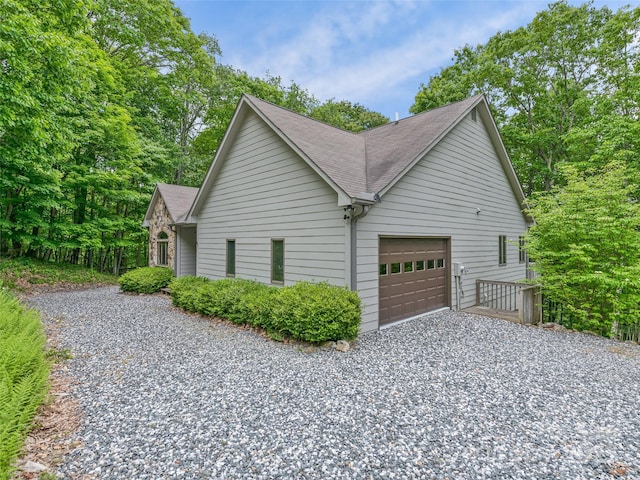 view of property exterior featuring an attached garage, roof with shingles, and gravel driveway
