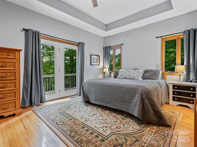 bedroom with a tray ceiling, access to outside, a ceiling fan, and light wood-style flooring