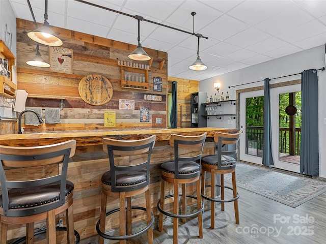 bar featuring wood walls, wood finished floors, a sink, wet bar, and decorative light fixtures