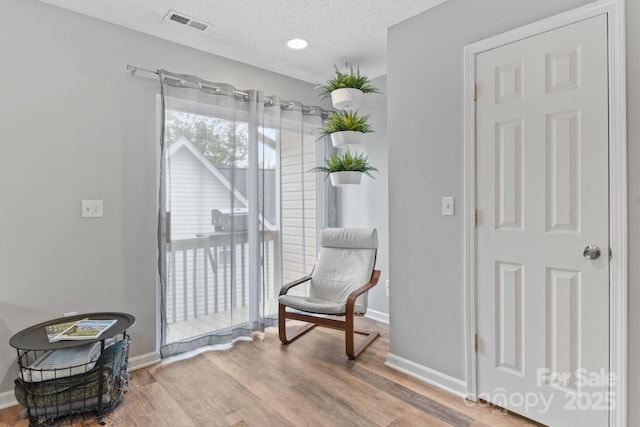 living area with a textured ceiling, visible vents, wood finished floors, and baseboards