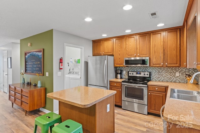 kitchen with a sink, light wood-style floors, stainless steel appliances, light countertops, and washer and dryer