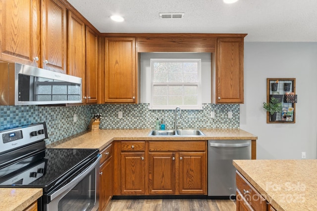 kitchen featuring stainless steel appliances, light wood-style floors, brown cabinets, a sink, and visible vents