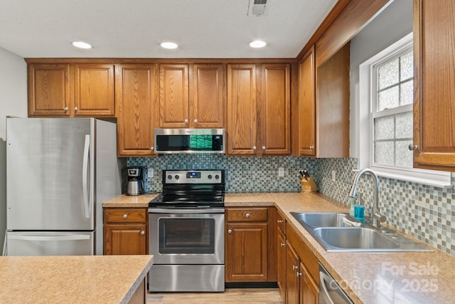 kitchen with brown cabinets, stainless steel appliances, light countertops, and a sink