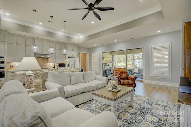 living room with ceiling fan, crown molding, light hardwood / wood-style floors, and a tray ceiling