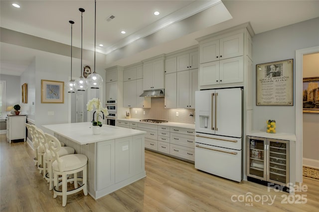 kitchen featuring a center island with sink, appliances with stainless steel finishes, backsplash, wine cooler, and hanging light fixtures