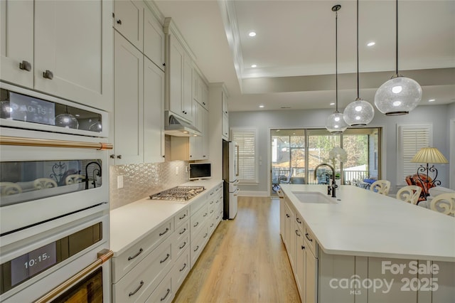 kitchen with decorative backsplash, sink, hanging light fixtures, a kitchen island with sink, and appliances with stainless steel finishes