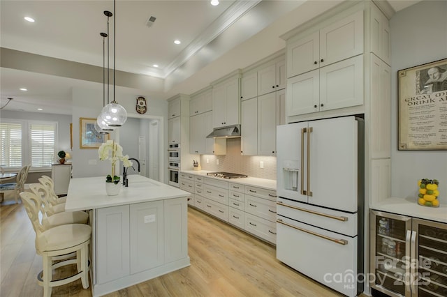 kitchen with beverage cooler, decorative light fixtures, stainless steel appliances, an island with sink, and a raised ceiling