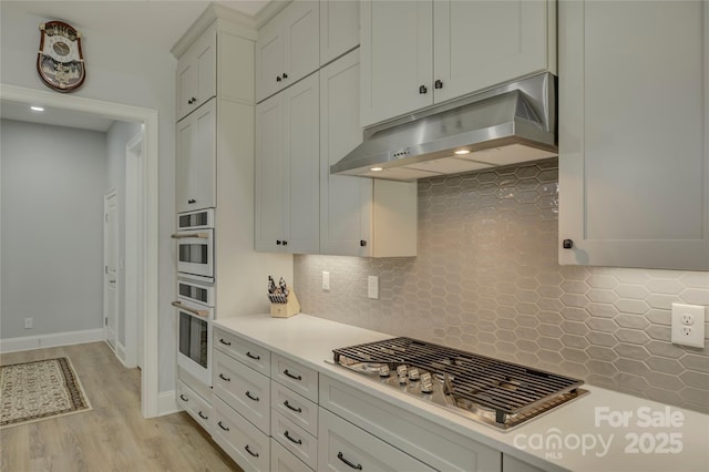 kitchen with stainless steel gas cooktop, decorative backsplash, light hardwood / wood-style flooring, and white cabinets