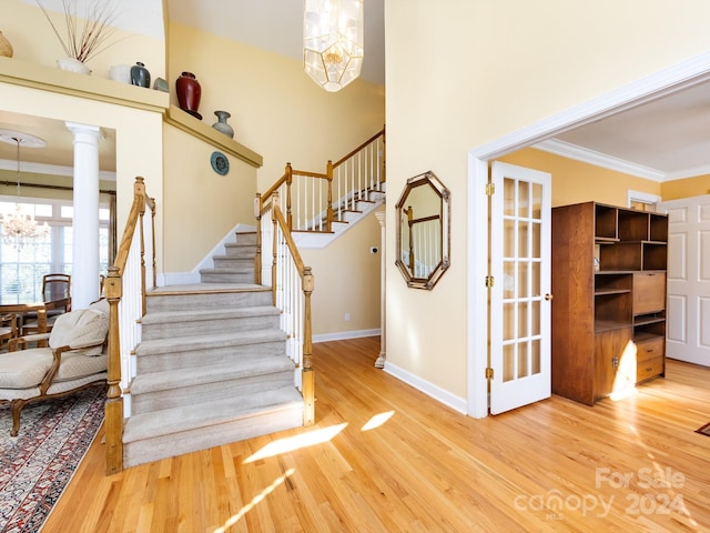 staircase featuring hardwood / wood-style floors, decorative columns, crown molding, and a chandelier