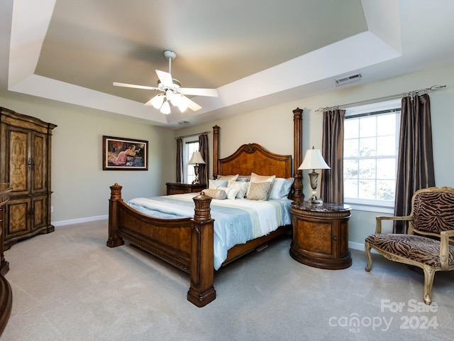 bedroom featuring light carpet, a tray ceiling, and ceiling fan