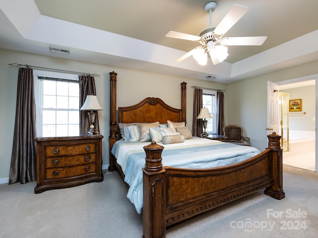 bedroom with a raised ceiling, multiple windows, ensuite bathroom, and ceiling fan