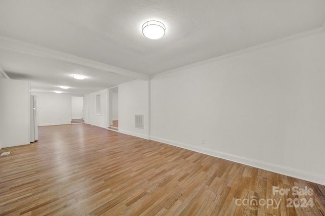 empty room featuring a textured ceiling, light hardwood / wood-style flooring, and crown molding