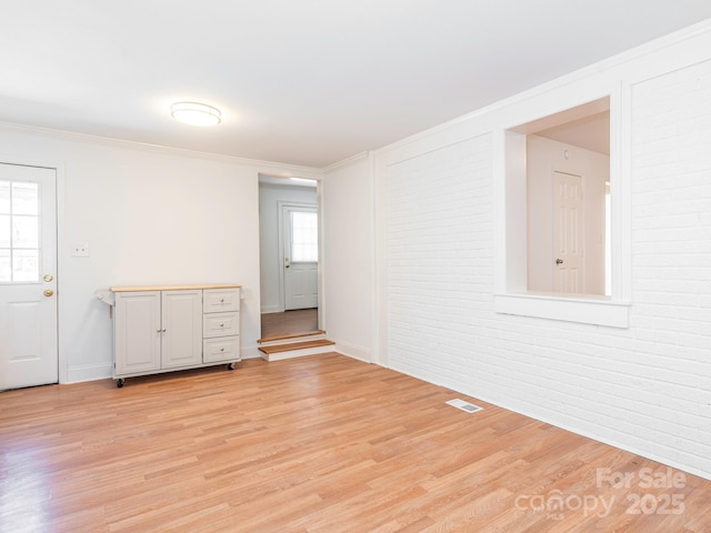 spare room with crown molding, visible vents, light wood-style flooring, brick wall, and baseboards