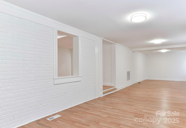 spare room featuring brick wall, wood finished floors, and visible vents