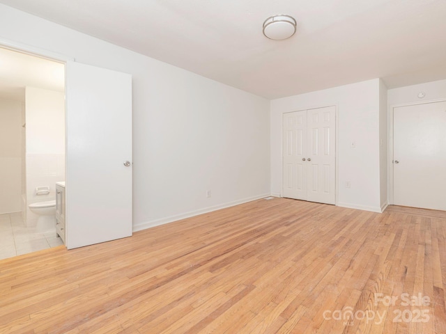 unfurnished bedroom with a closet, light wood-style flooring, baseboards, and ensuite bathroom