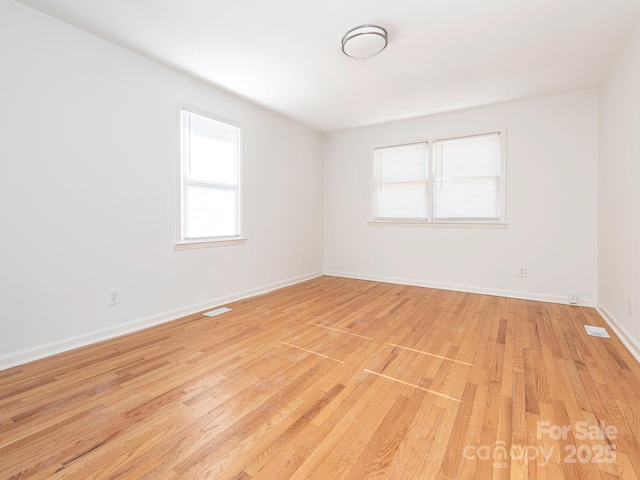 unfurnished room with light wood-type flooring, visible vents, and baseboards