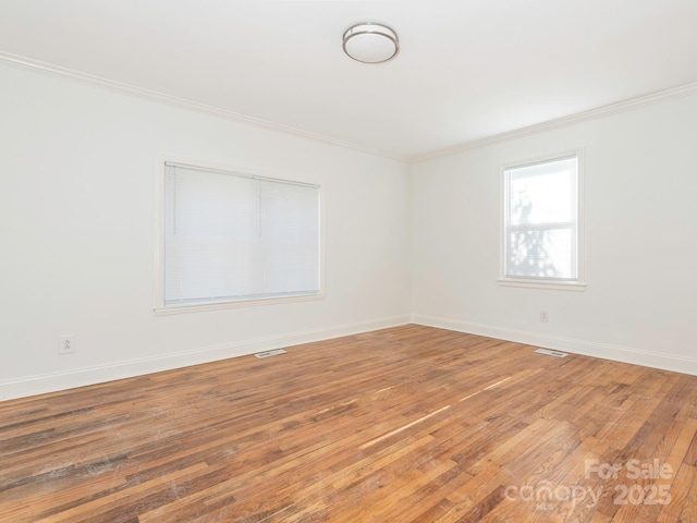 unfurnished room featuring baseboards, hardwood / wood-style floors, visible vents, and crown molding