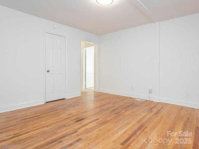 spare room featuring light wood-type flooring, visible vents, and baseboards