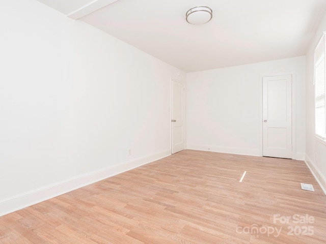 spare room with light wood-type flooring, visible vents, and baseboards