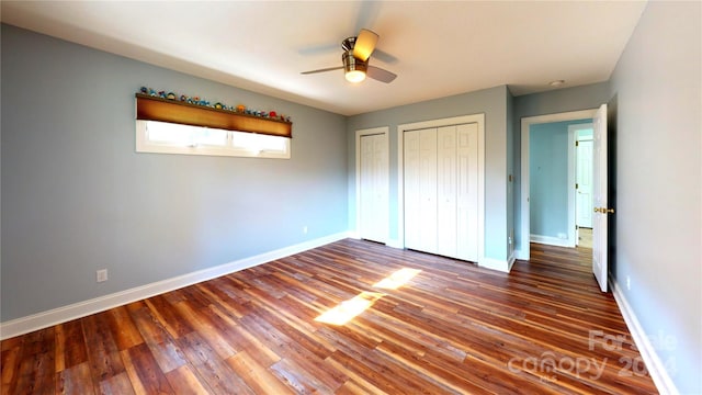 unfurnished bedroom with two closets, dark hardwood / wood-style floors, and ceiling fan