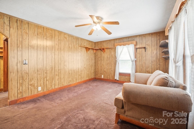 living area with ceiling fan, wooden walls, and carpet