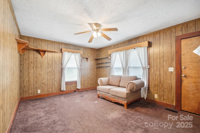 unfurnished room featuring wooden walls, dark carpet, a textured ceiling, and ceiling fan