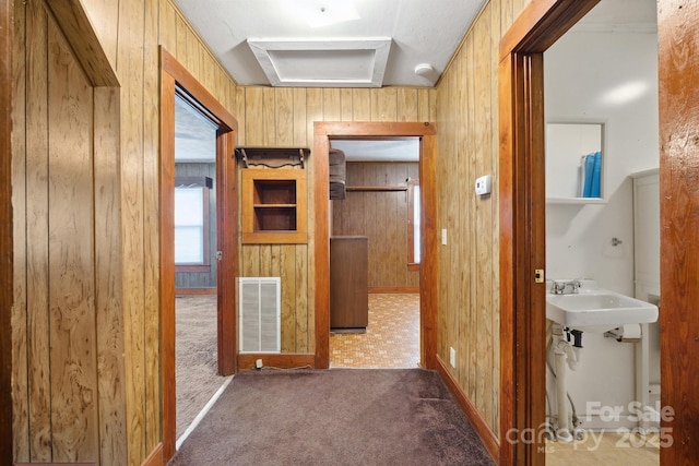 hall with sink, wooden walls, and dark colored carpet