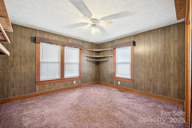 carpeted empty room with wooden walls and ceiling fan