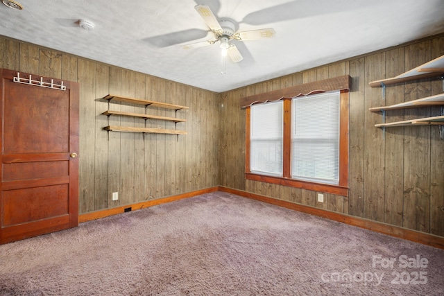 carpeted spare room featuring ceiling fan, wood walls, and a textured ceiling